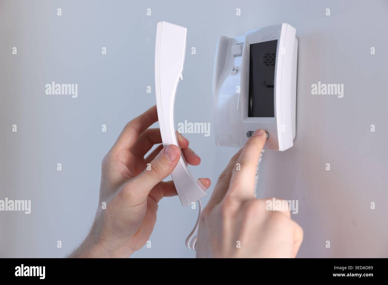 Man with handset pressing button on intercom panel indoors, closeup Stock Photo