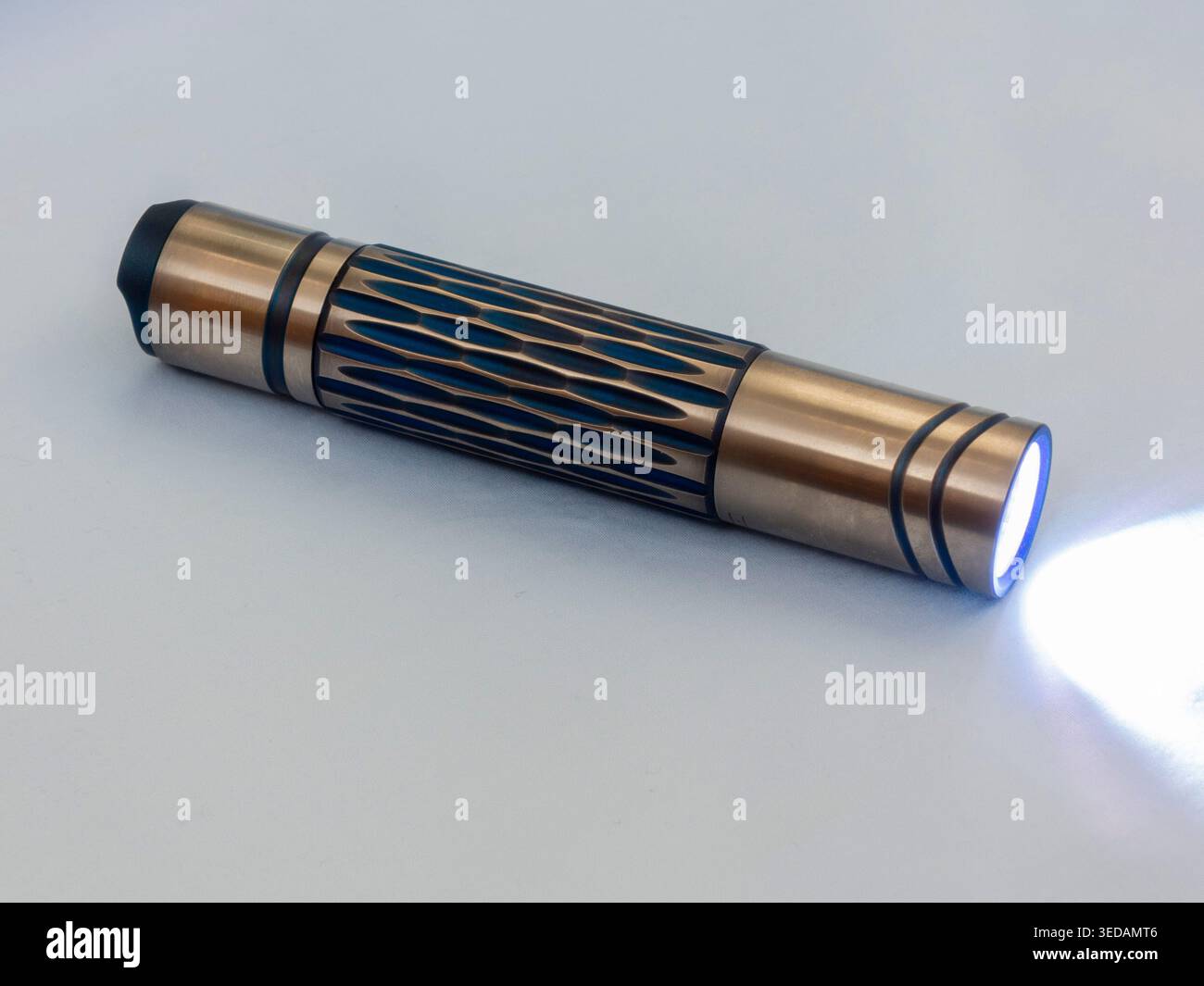 Titanium handheld flashlight on sky blue background Stock Photo