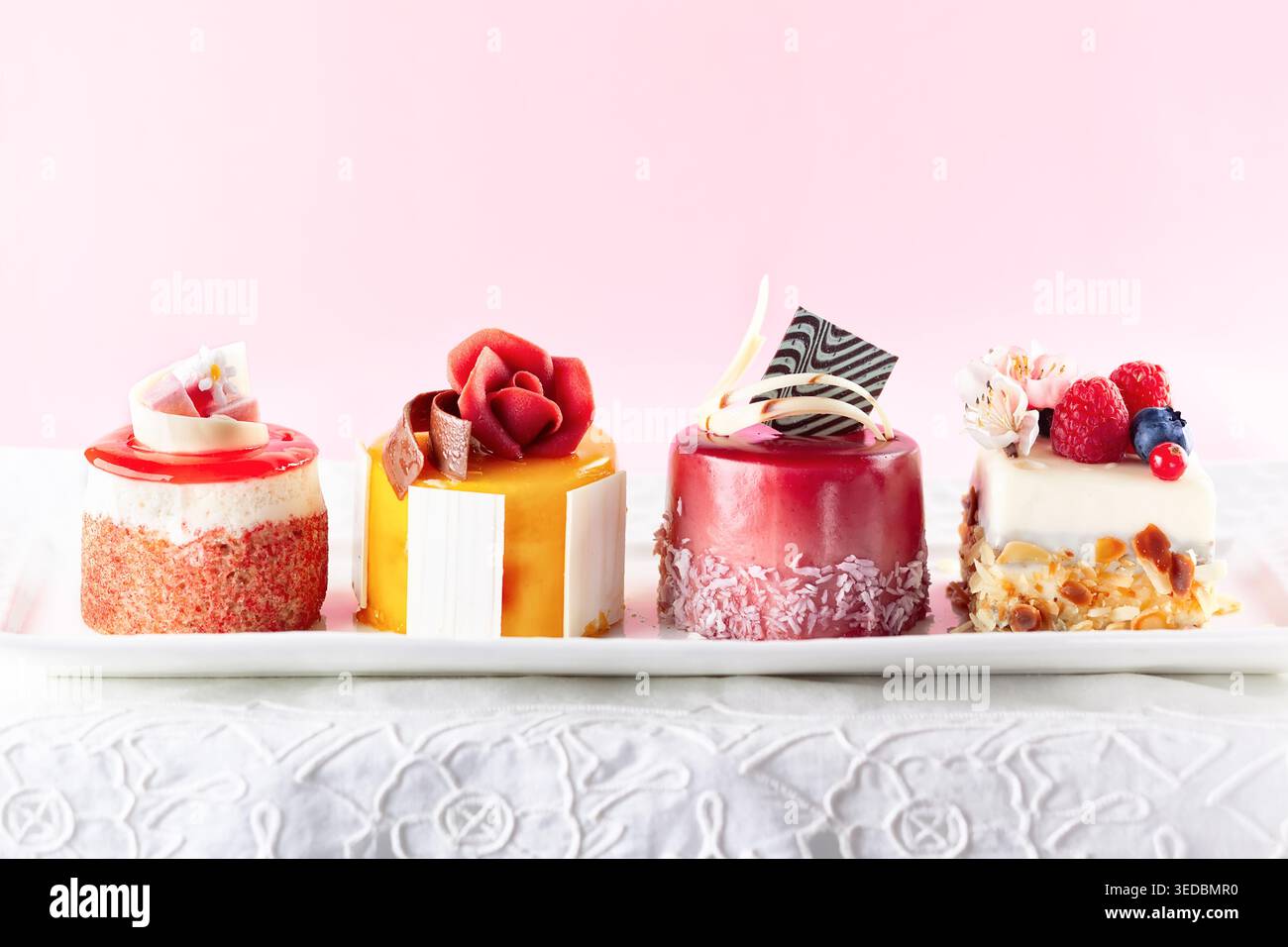 Various mini cakes on a white plate. Sweets decorated with fresh berries and flowers for holiday. Stock Photo
