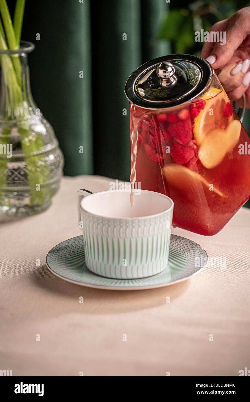 Pouring fruit tea from glass teapot into cup Stock Photo