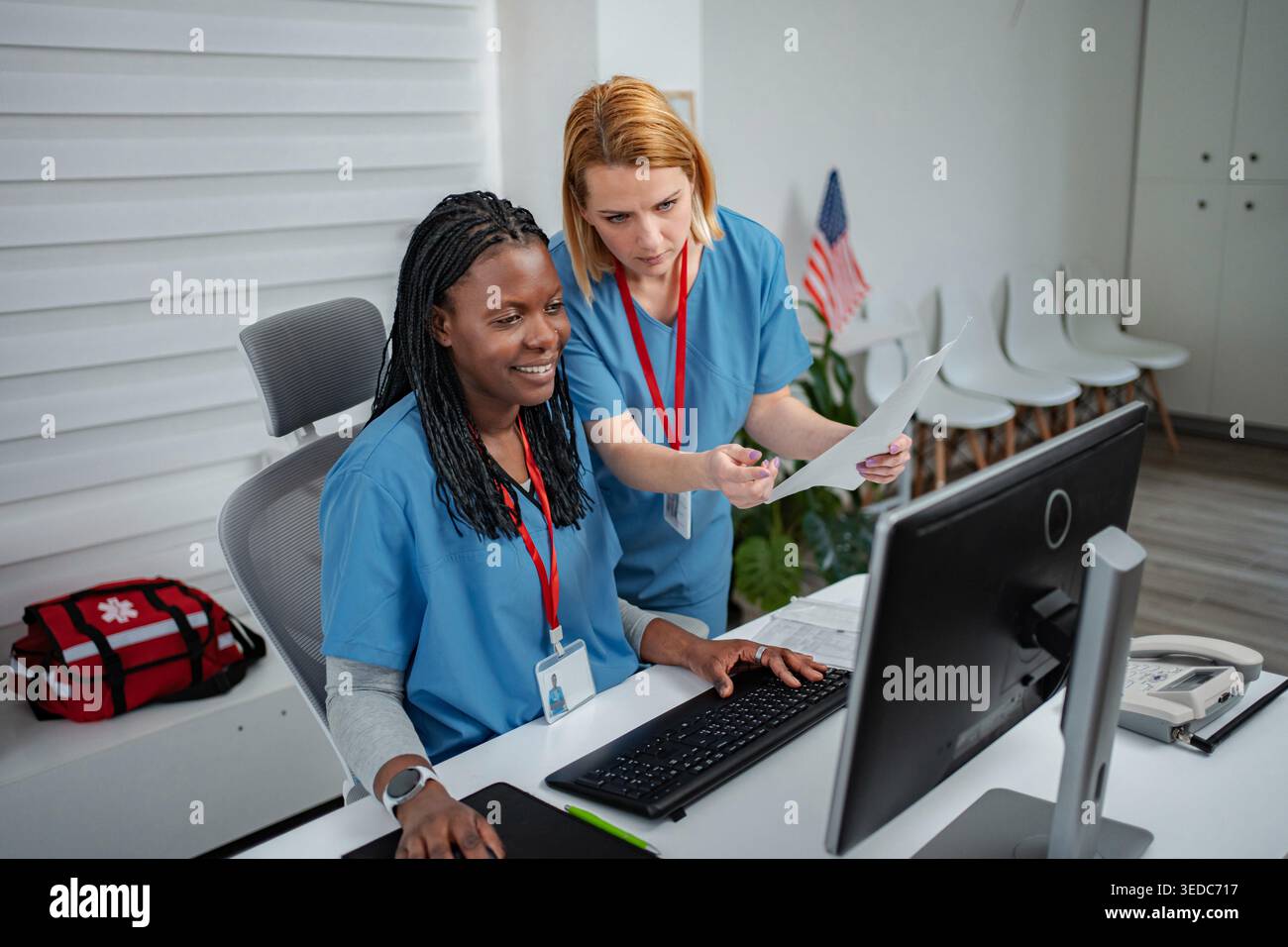 Two female nurses discussing patient information at a computer workstation Stock Photo