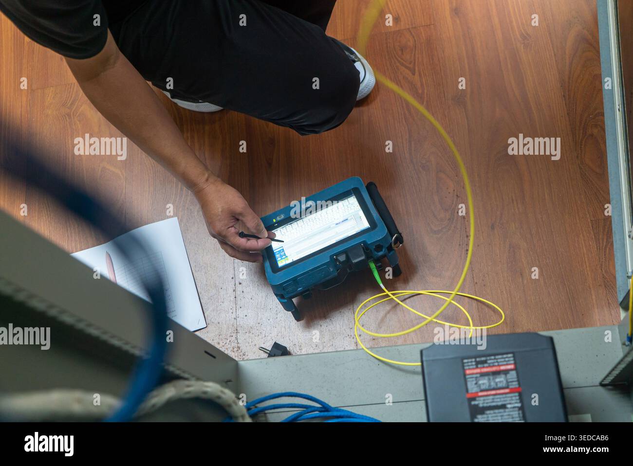 A technician carefully tests network equipment using a cable tester, showcasing hands-on analysis in a modern workspace with digital tools. Stock Photo