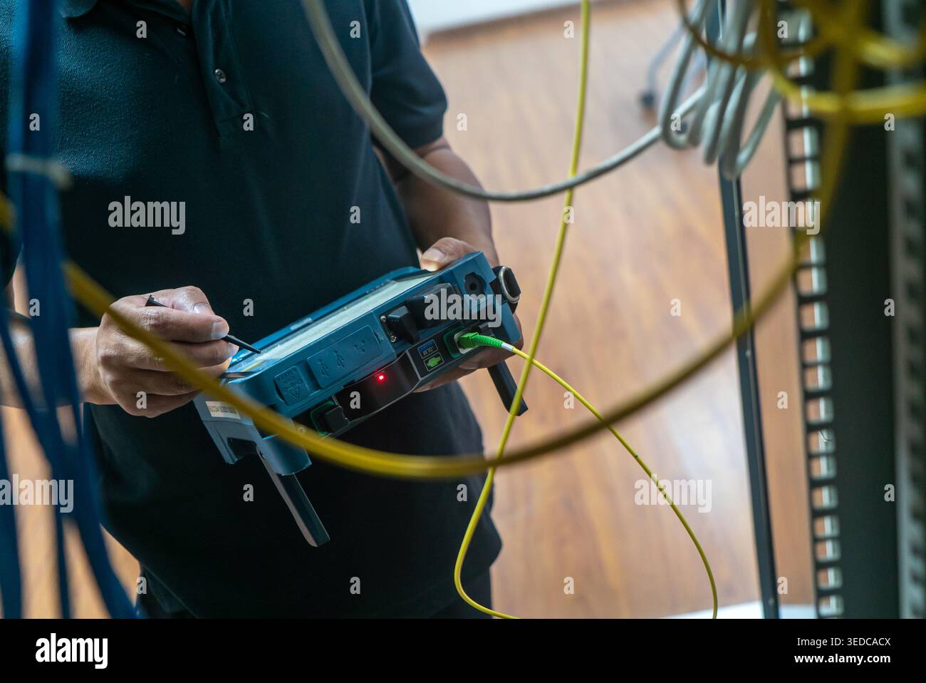 A technician carefully tests network equipment among tangled cables and wires in a modern workspace, ensuring proper functionality and connectivity. Stock Photo