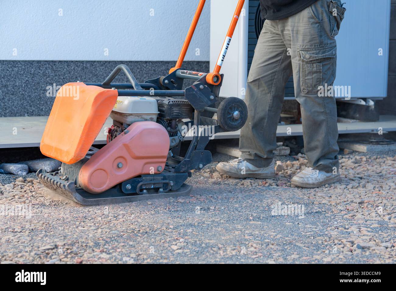 Worker uses a vibratory plate compactor for preparing a base layer. Essential step before paving, decking, or foundation installation. Stock Photo