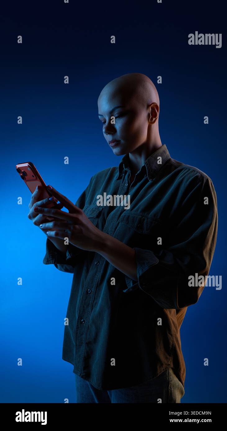 Thoughtful woman browsing smartphone under blue studio light Stock Photo