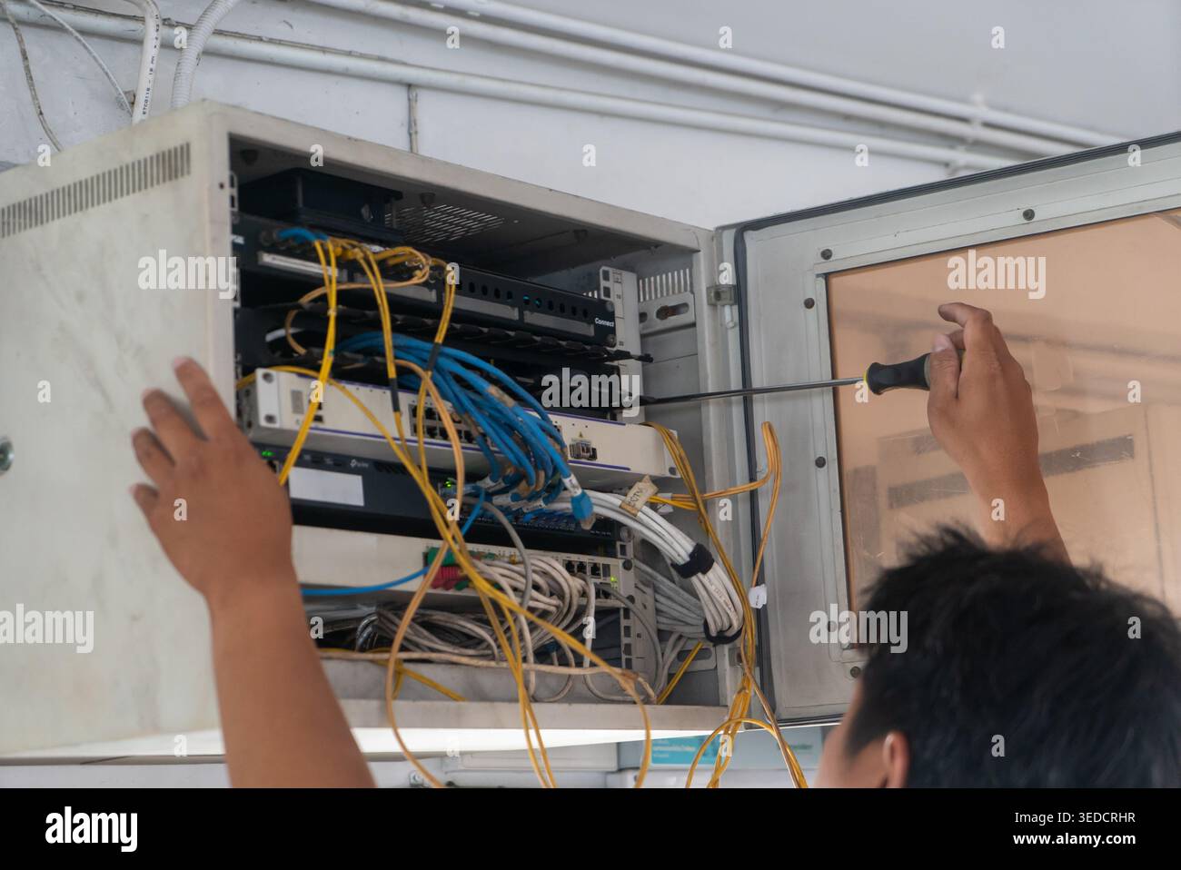 A technician performing maintenance on a server cabinet, managing cables and connections. The image showcases hands at work with tools in a tech envir Stock Photo