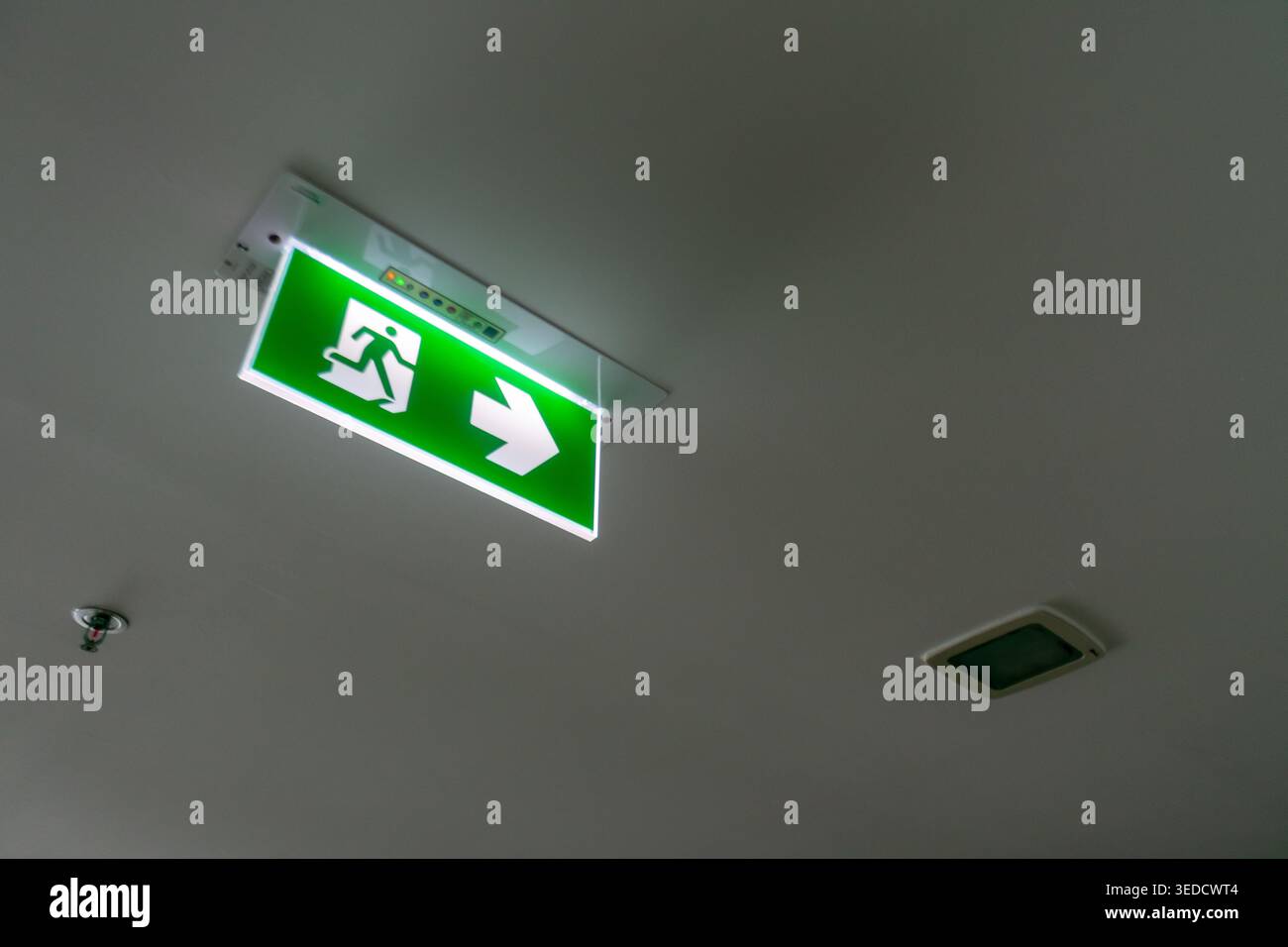 A bright green emergency exit sign with an arrow is mounted on the ceiling, providing clear direction for safe evacuation in case of emergencies. Stock Photo