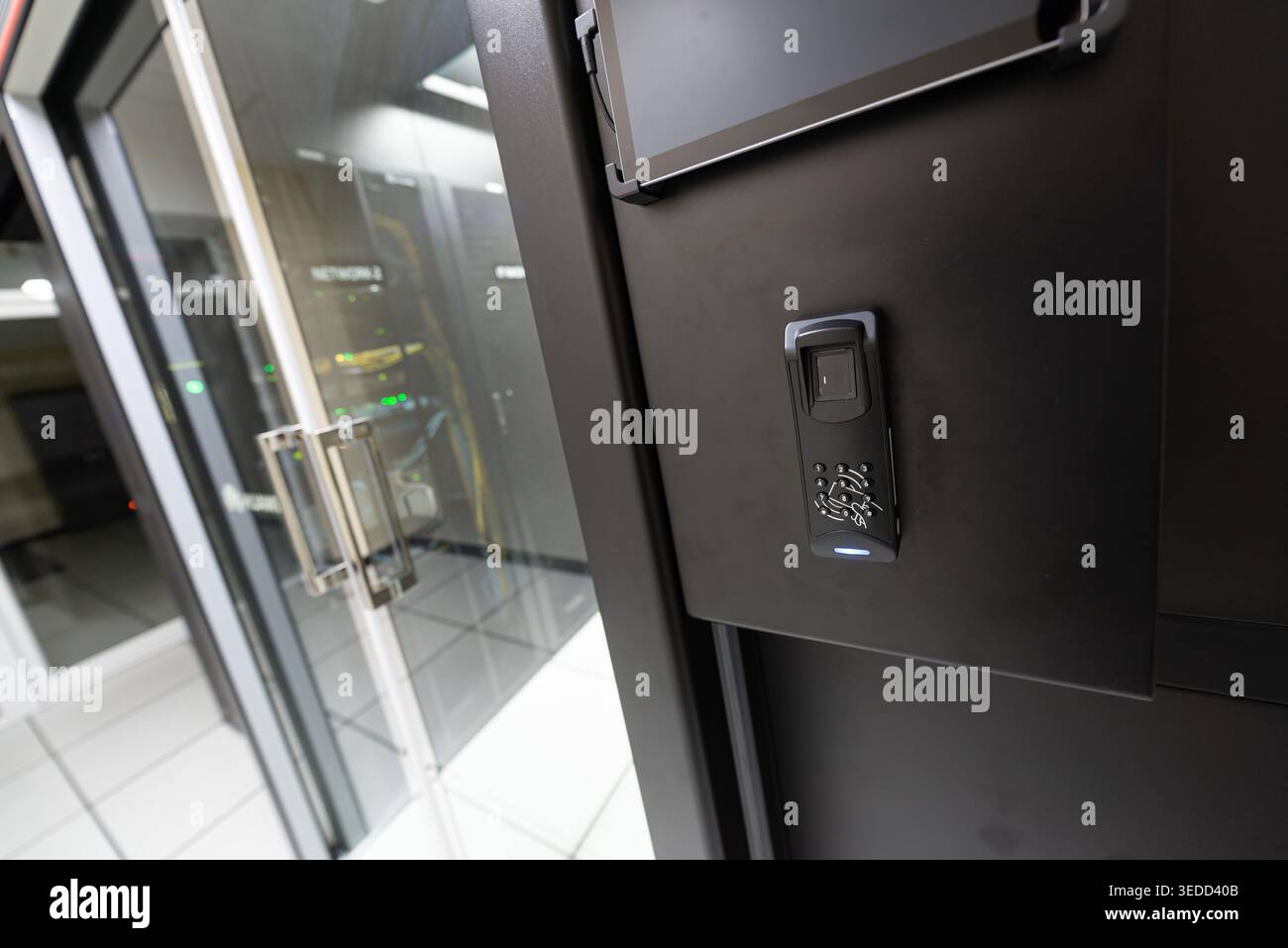 This image showcases a secure access control system at a data center, featuring a biometric fingerprint scanner next to a modern glass door entrance. Stock Photo