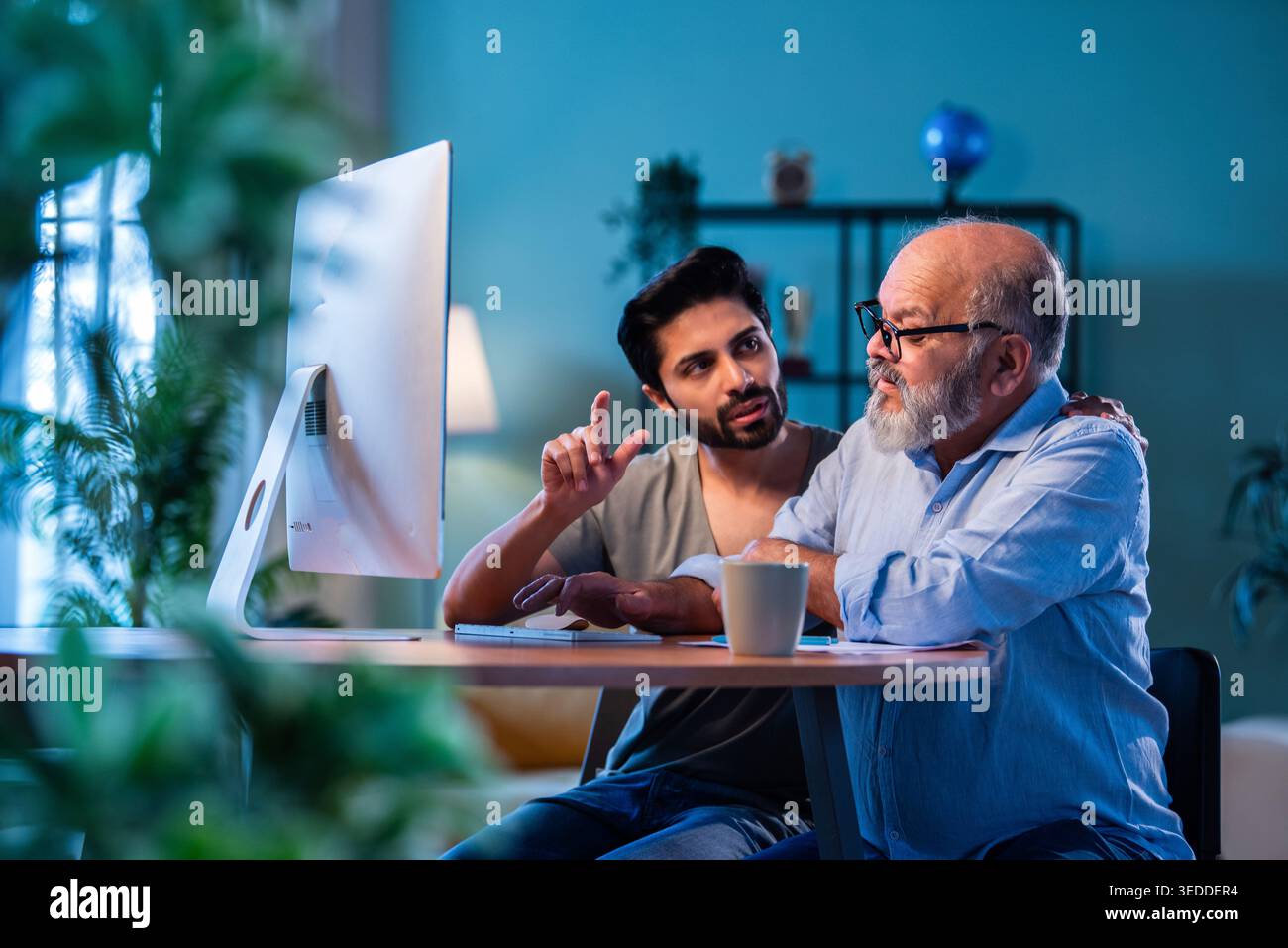 Indian young son teaching senior father how to use desktop computer at ...