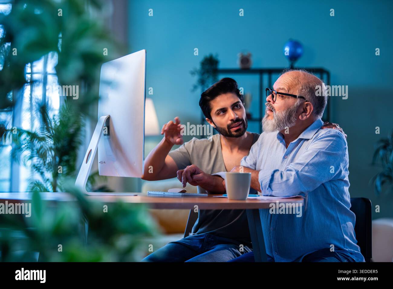 Indian young son teaching senior father how to use desktop computer at ...