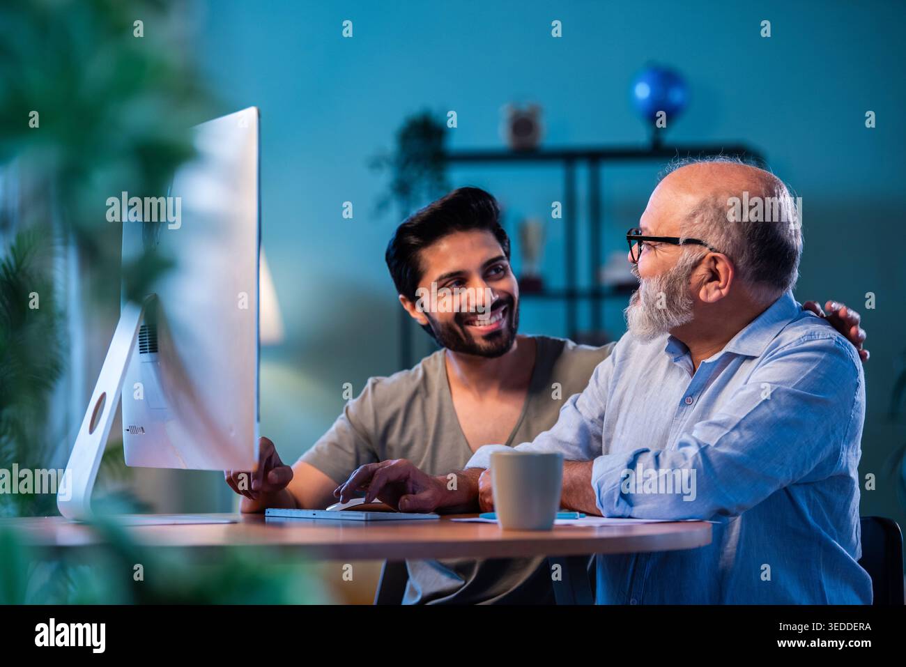 Indian young son teaching senior father how to use desktop computer at ...