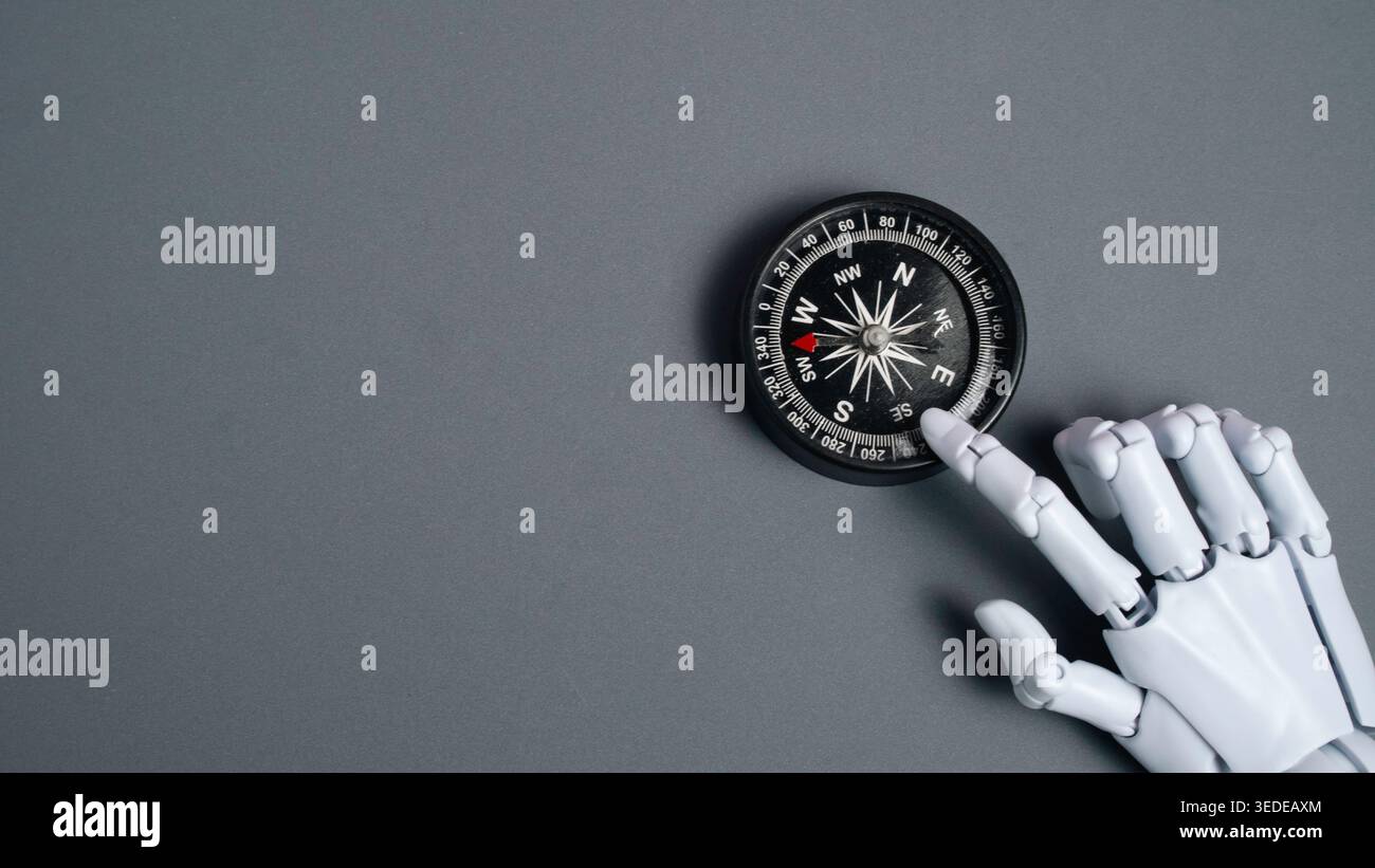 Robot finger pointing at a black magnetic compass on a grey background ...