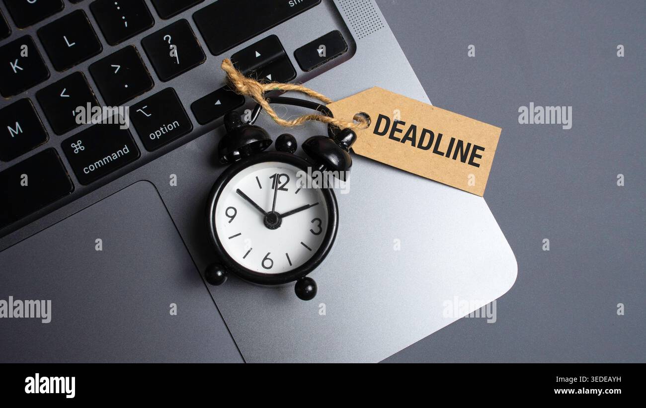 Deadline Tag on Small Black Alarm Clock Placed on Laptop Keyboard Representing Work Pressure and Time Constraints Stock Photo
