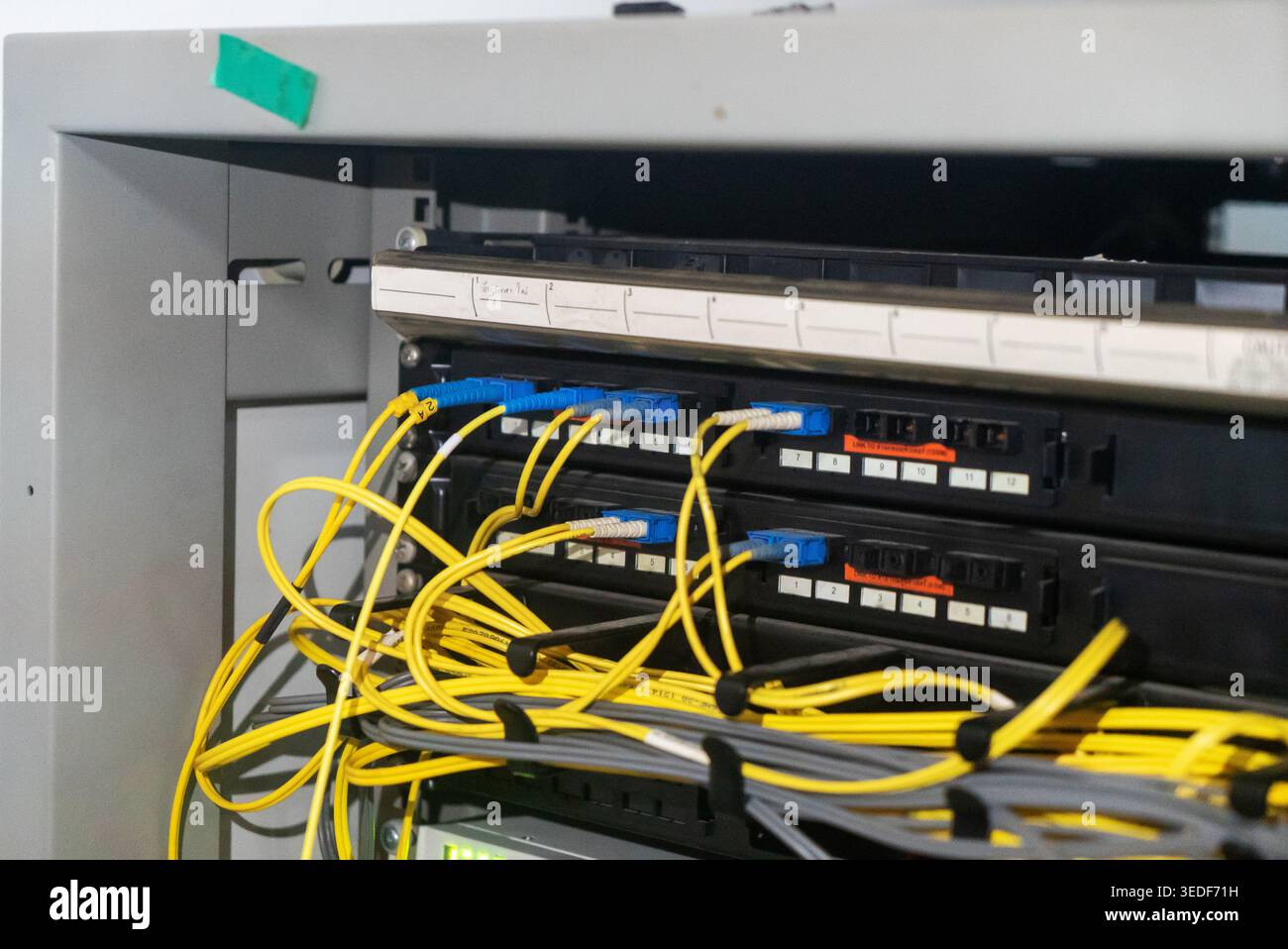 Close-up of a server rack displaying organized fiber optic cables in vibrant yellow and blue. Ideal for tech, network, and data communication concepts Stock Photo