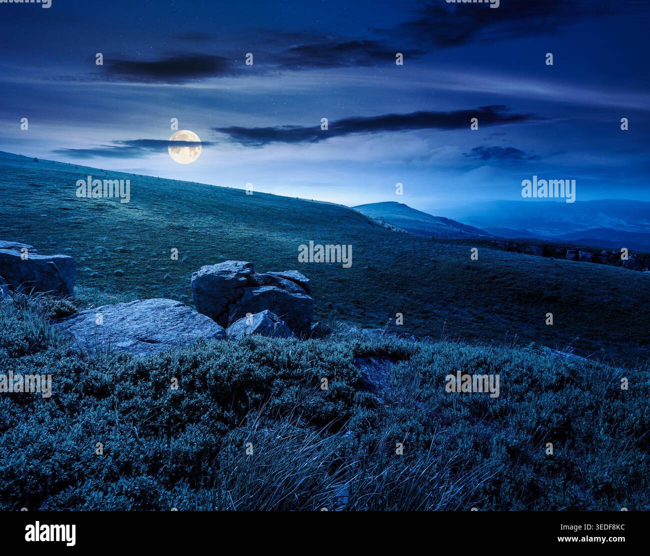 mountain summer landscape at night. full moon over meadow with giant stones among the grass on the hillside. mysterious view near the peak of mountain Stock Photo
