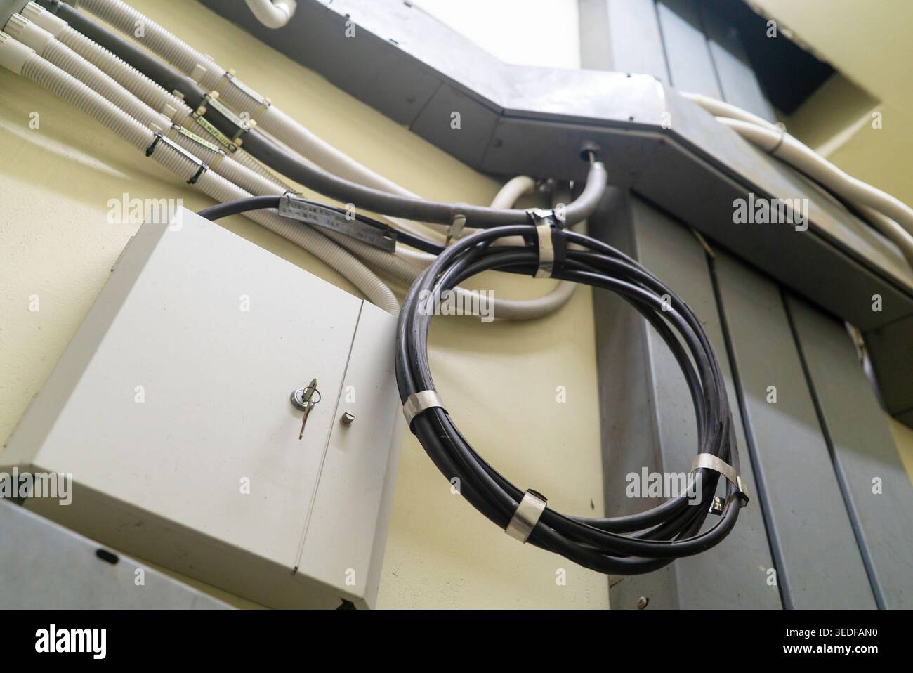 This image shows a wire management system featuring a looped cable secured to a wall-mounted junction cabinet, representing efficient organization and Stock Photo