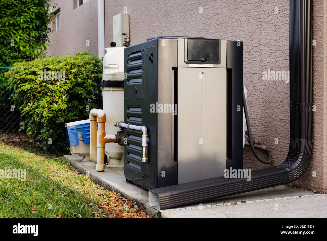 Modern natural gas swimming pool heater unit and pool water filtration equipment on concrete slab outside of house. Stock Photo