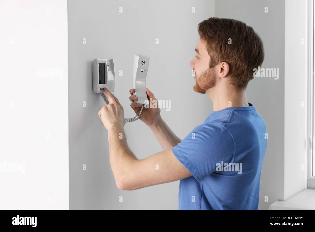 Man with handset pressing button on intercom panel indoors Stock Photo