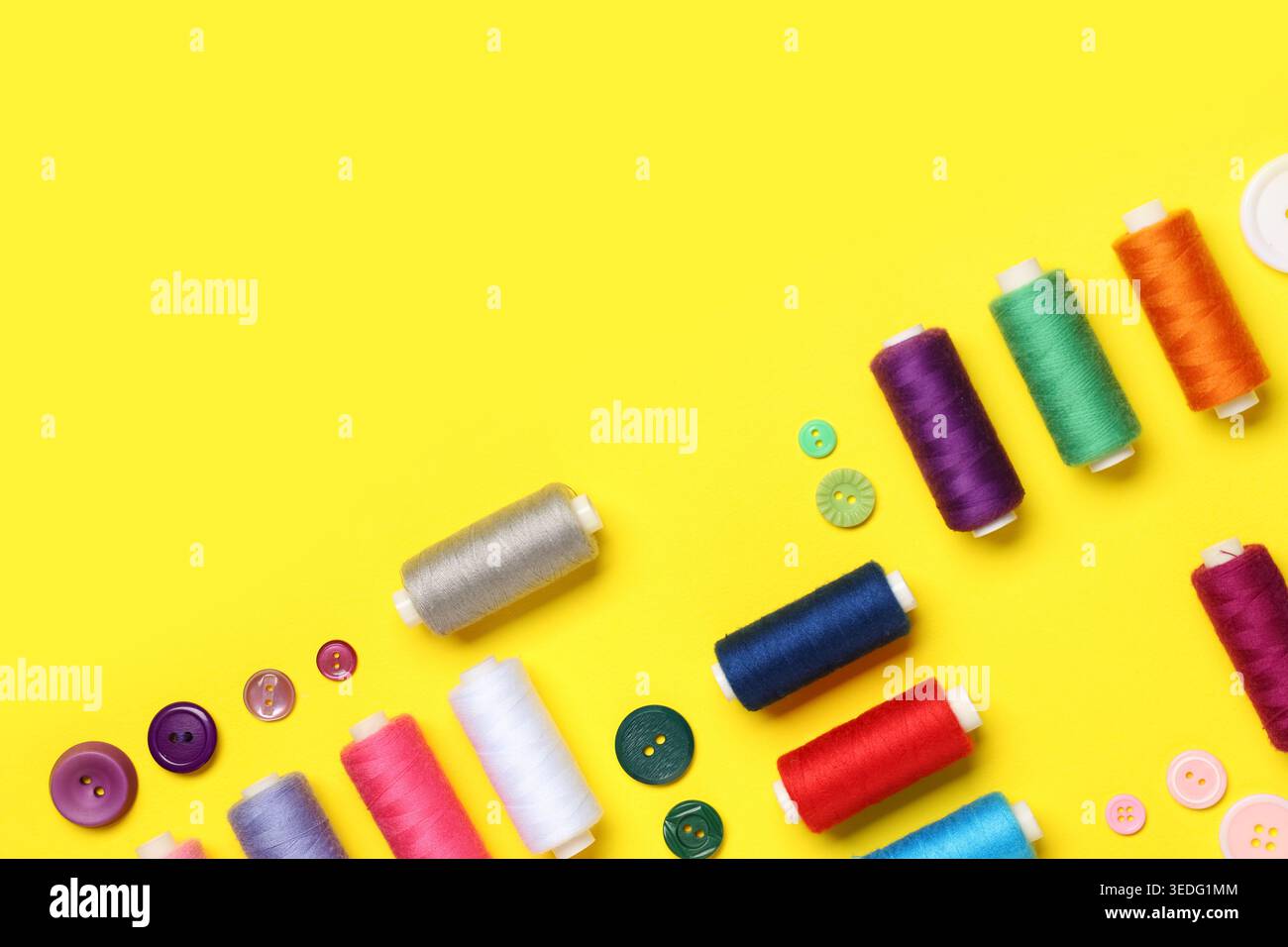 Composition with many different thread spools and buttons on yellow background Stock Photo
