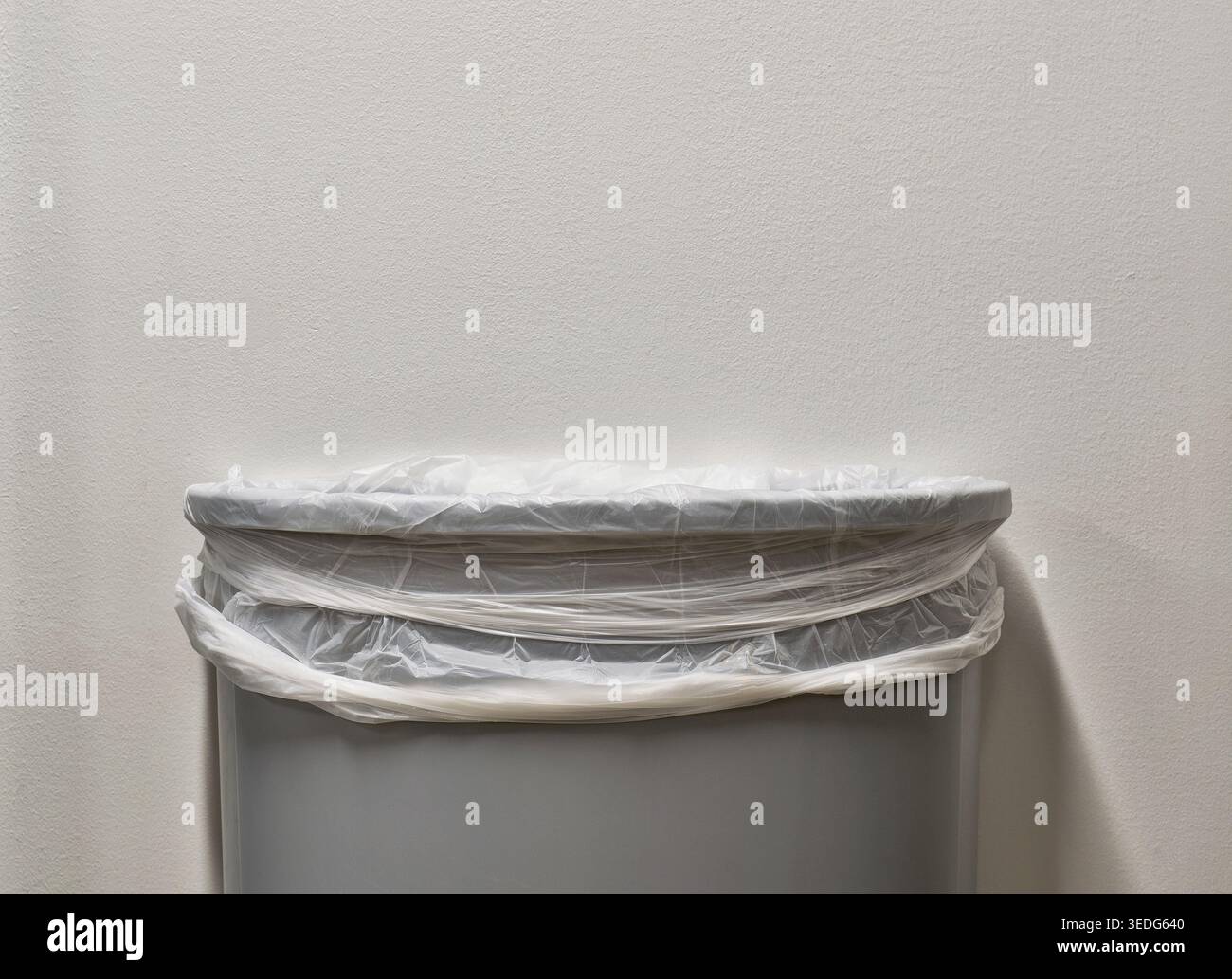 Gray trashcan partial with trash bin liner by white plain wall with copy space. Stock Photo
