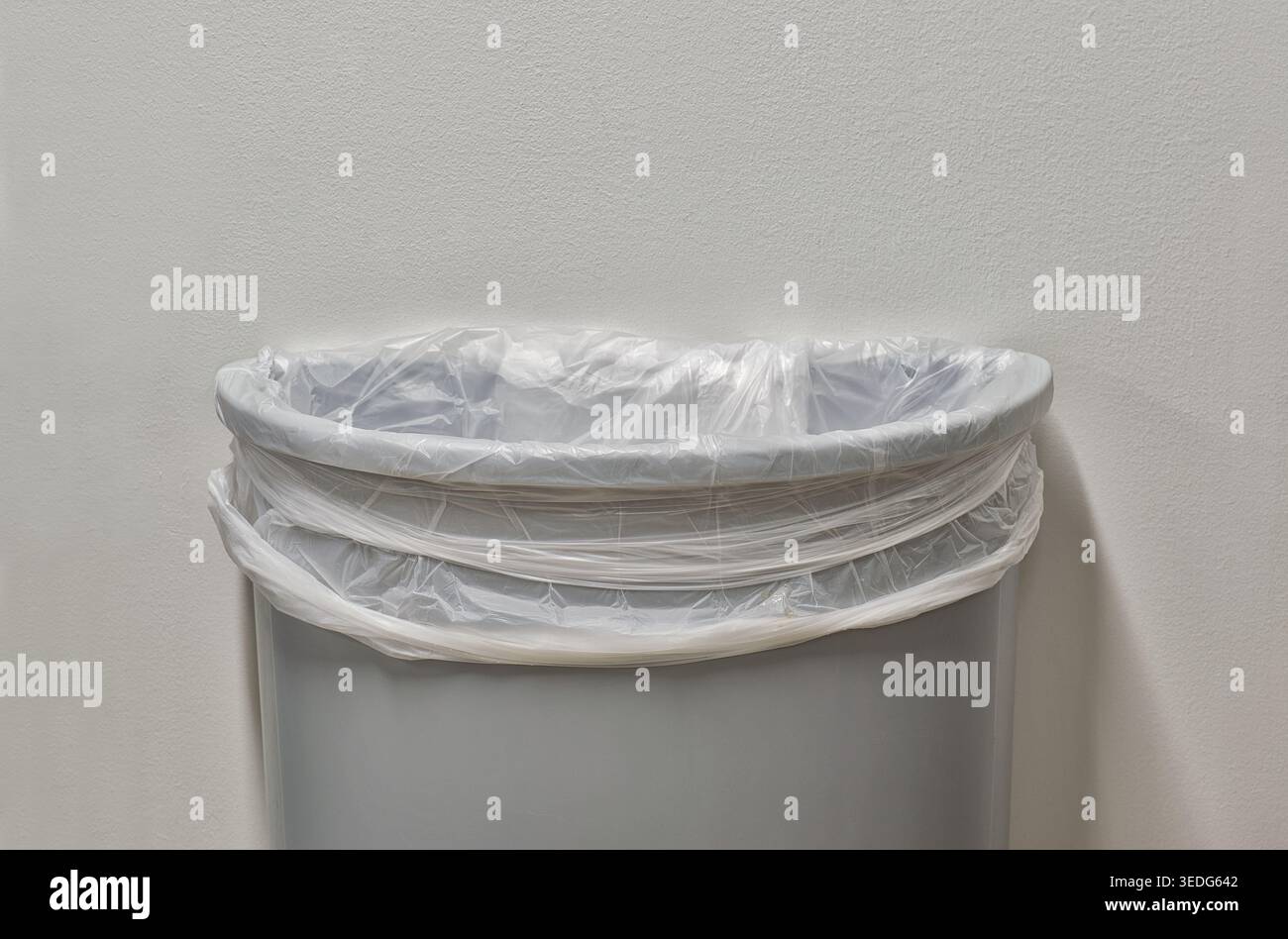 Gray trashcan partial with trash bin liner by white plain wall with copy space. Stock Photo