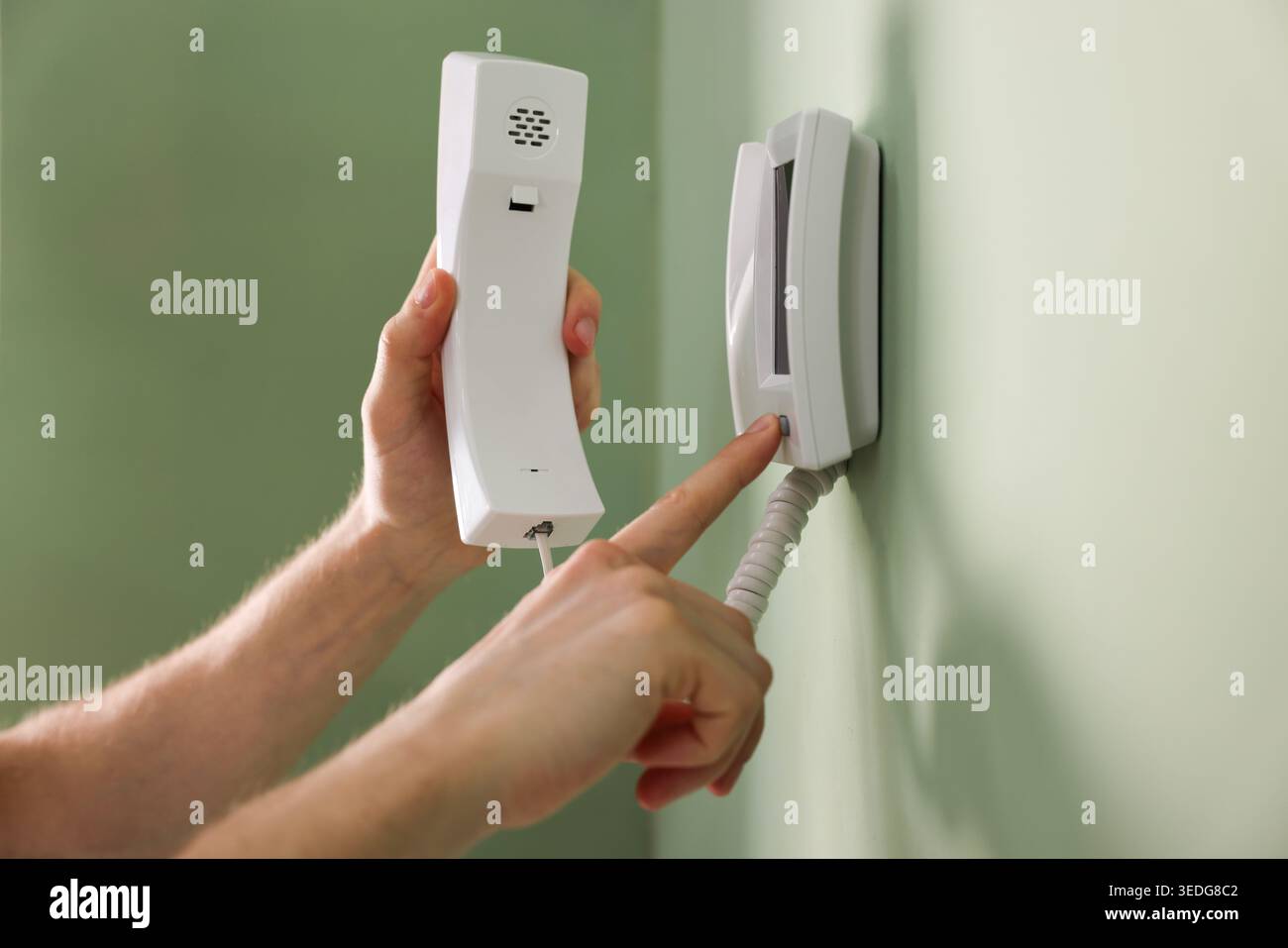 Man with handset pressing button on intercom panel indoors, closeup Stock Photo