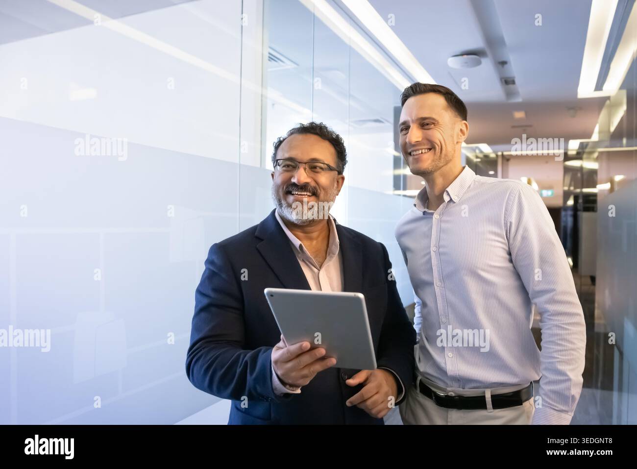 Team members stand in office hallway with digital tablet Stock Photo