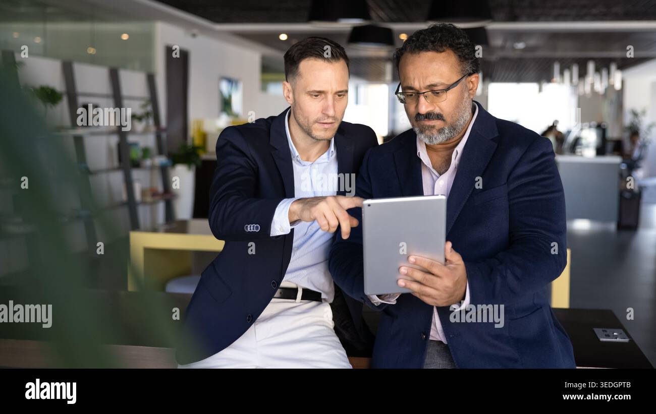 Two focused multiethnic businessmen analyzing information on digital tablet Stock Photo