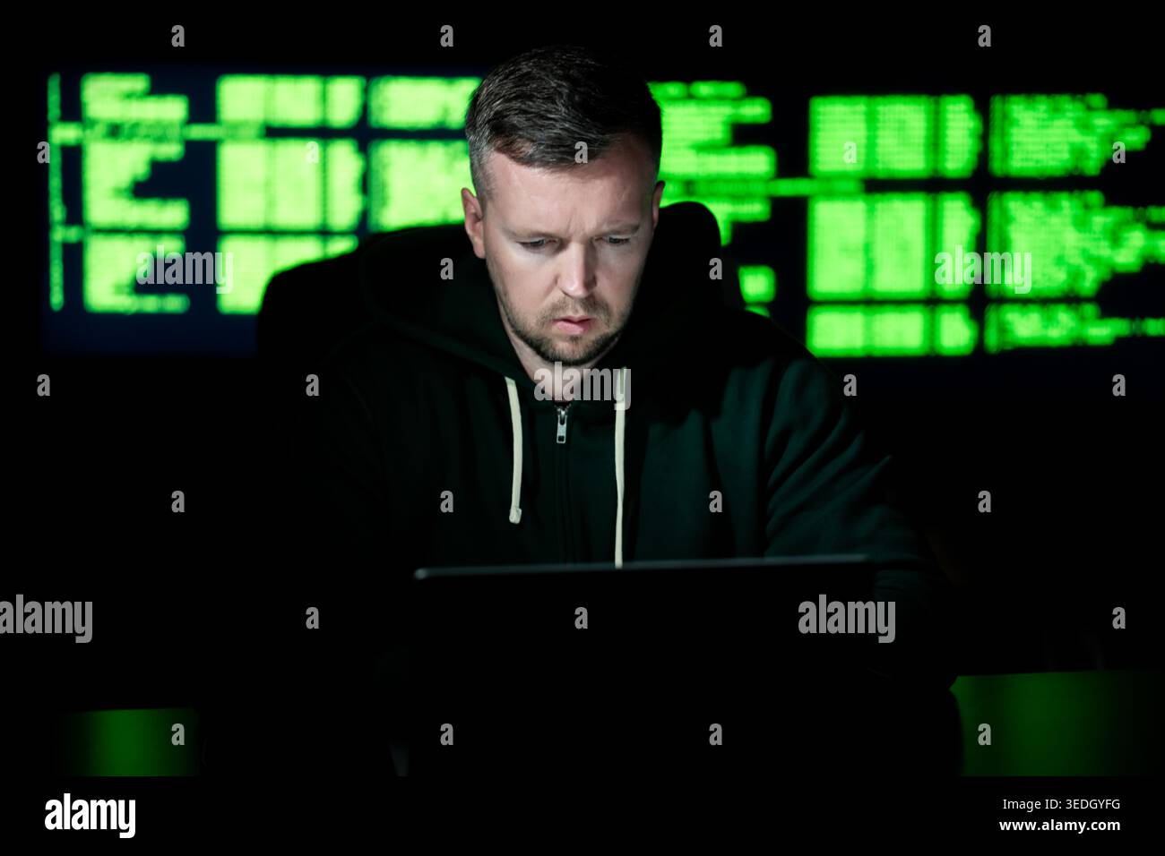 Hacker uses computer in dark room. Hacker analyzes system code and data. Hacker monitors secure network connections. Hacker executes cyber crime Stock Photo