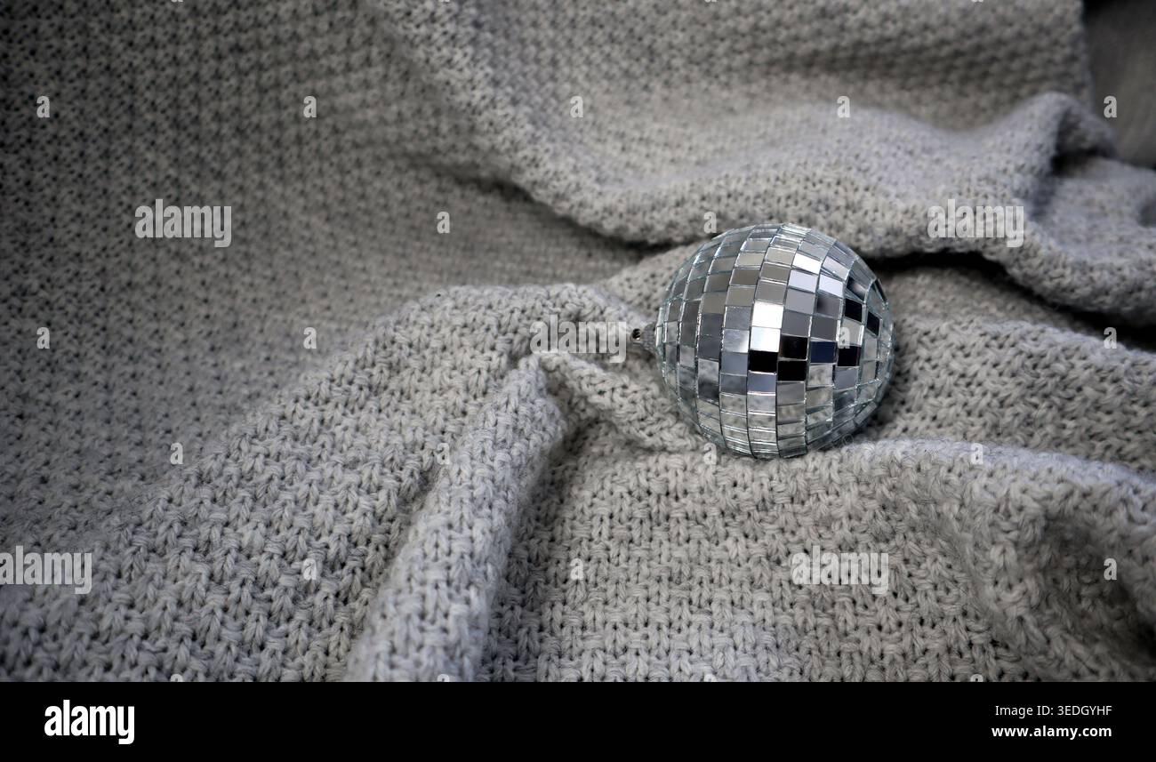 A disco ball sits on a soft gray fabric, reflecting light in a simple indoor space. The texture of the fabric contrasts with the shiny surface of the Stock Photo