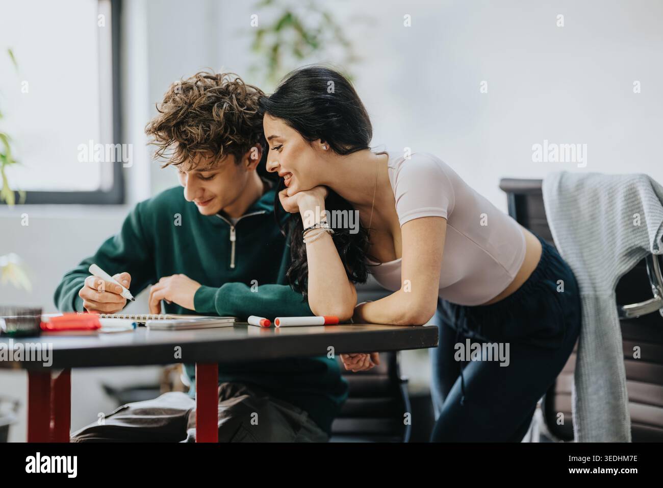 Two students studying together at a desk, smiling and collaborating on homework Stock Photo