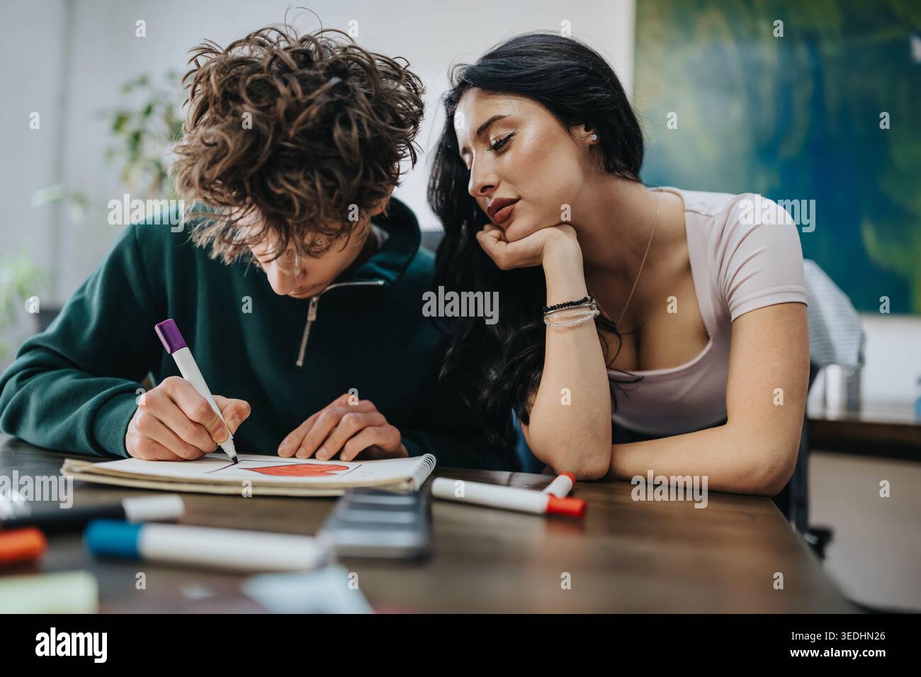 Two students collaborating on a drawing at a table while one guides the other Stock Photo