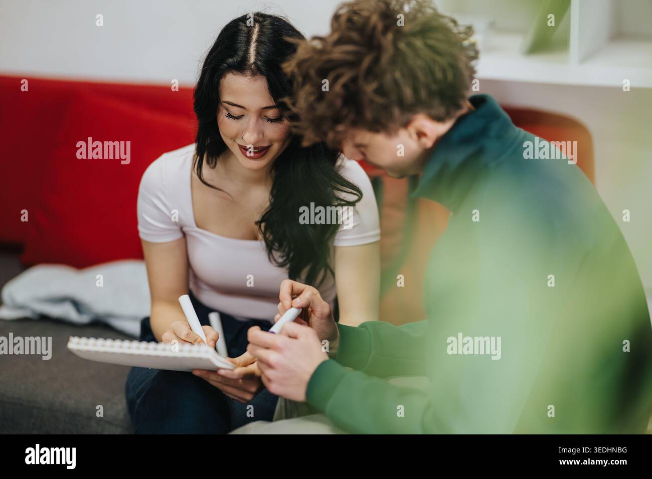 Two students studying together on a couch with notebook and markers, collaborating on notes Stock Photo