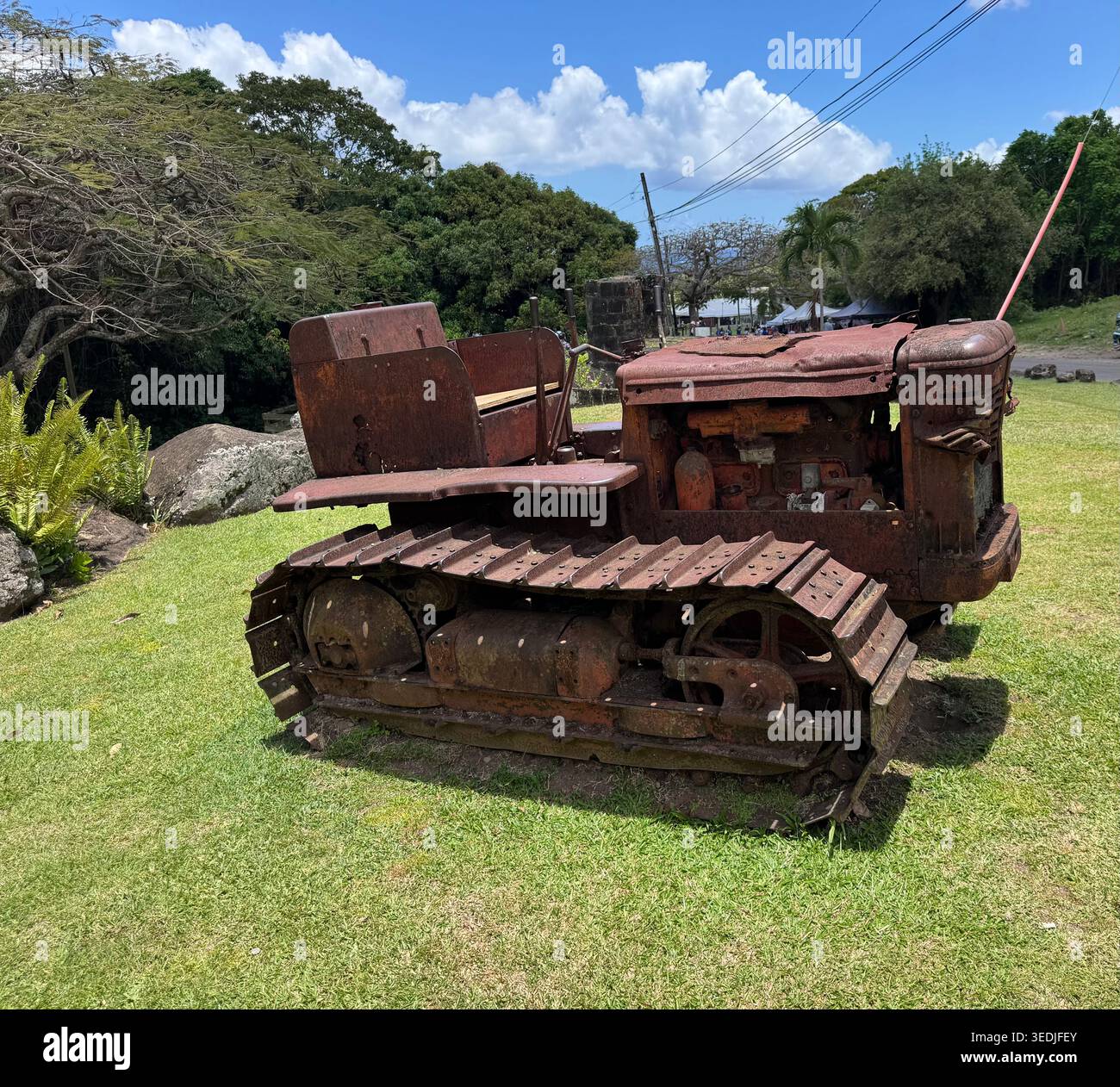 A vintage rusty crawler tractor vehicle displayed on a green grass field near a historic estate. - Smartphone Captured Stock Image