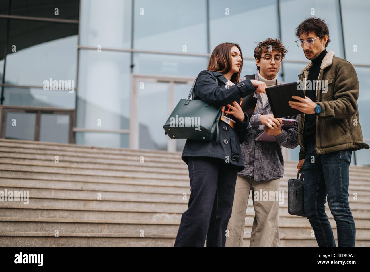 High school students collaborating with a tablet on campus steps during a casual study session Stock Photo