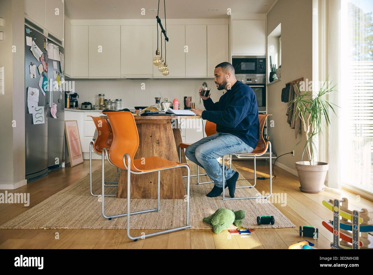 Male freelancer drinking coffee while working on laptop from home Stock Photo