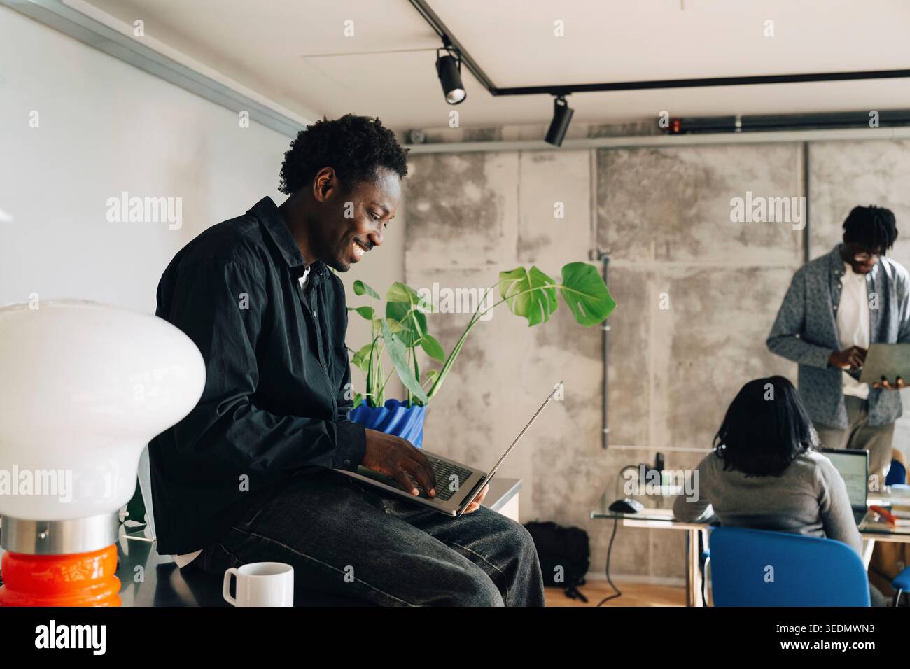 Smiling computer programmer working on laptop while sitting in modern startup office Stock Photo