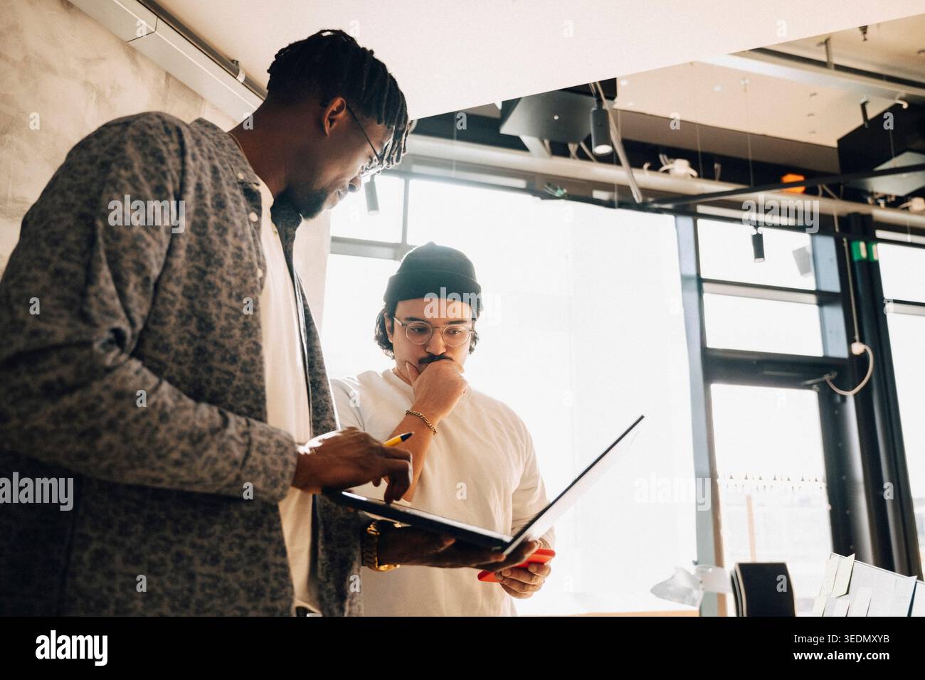 Male computer programmers discussing ideas while working on laptop at modern startup office Stock Photo