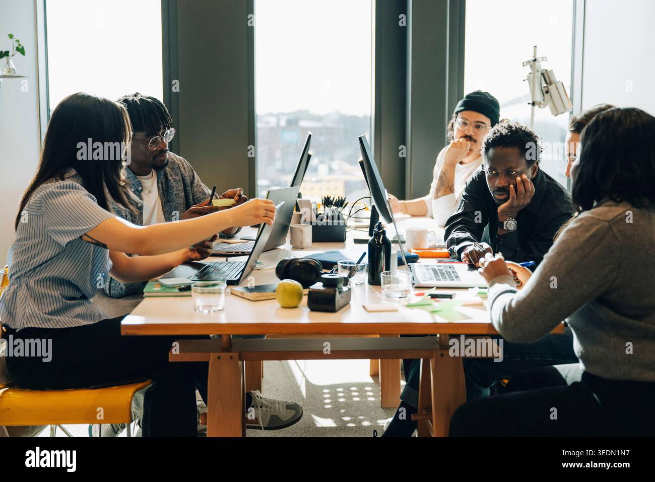 Diverse team of programmers working on laptops and computers while sitting around cluttered desk in office Stock Photo