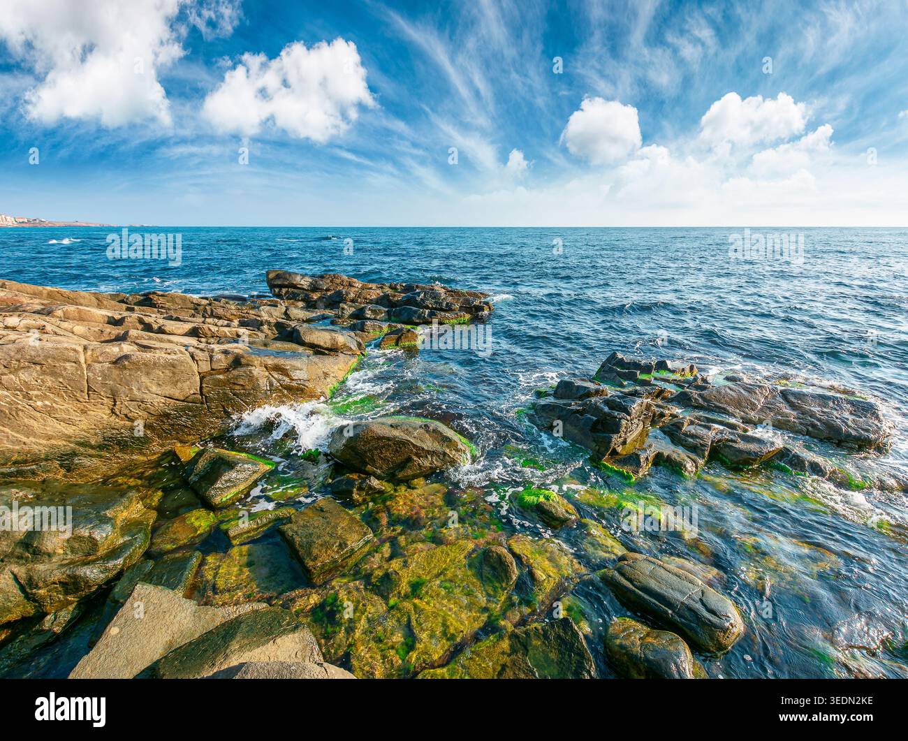 sea coast with stones and boulders in the forenoon. view of beach with rock in seaweed. dynamic cloudscape on the sky over horizon. summer vacations b Stock Photo