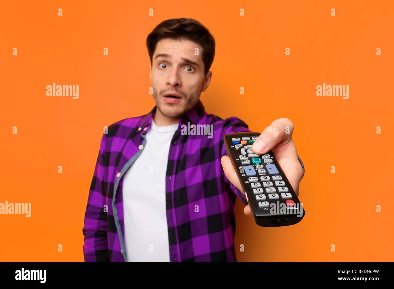 Man Holds Remote Control in a Studio With Orange Background During Evening Time Stock Photo