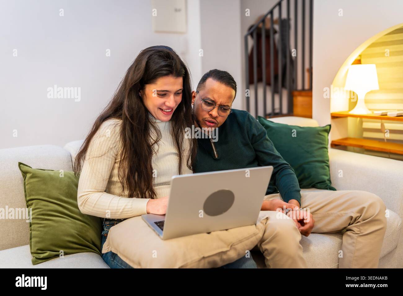 Interracial couple relaxing on sofa using laptop together Stock Photo