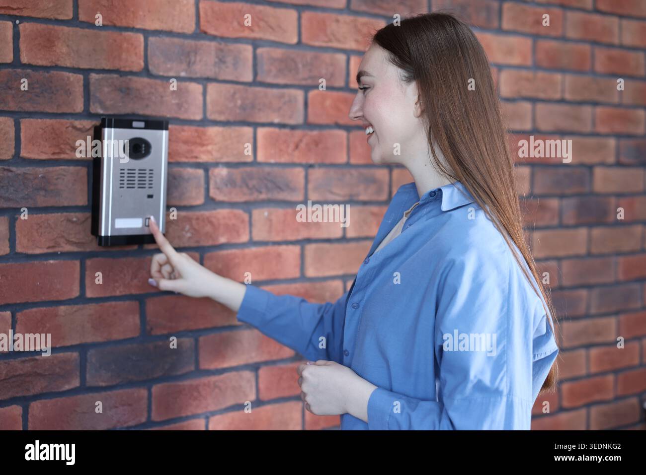 Woman pressing button on intercom panel near brick wall Stock Photo