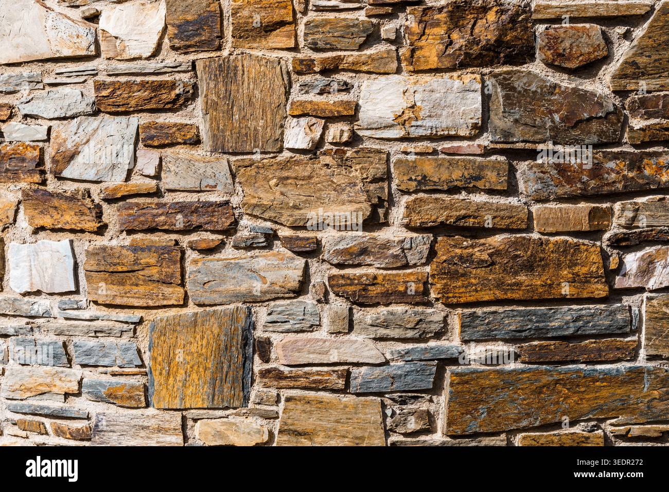Rustic stone wall featuring various natural rock shapes and colors, creating a textured surface. Perfect as a background Stock Photo