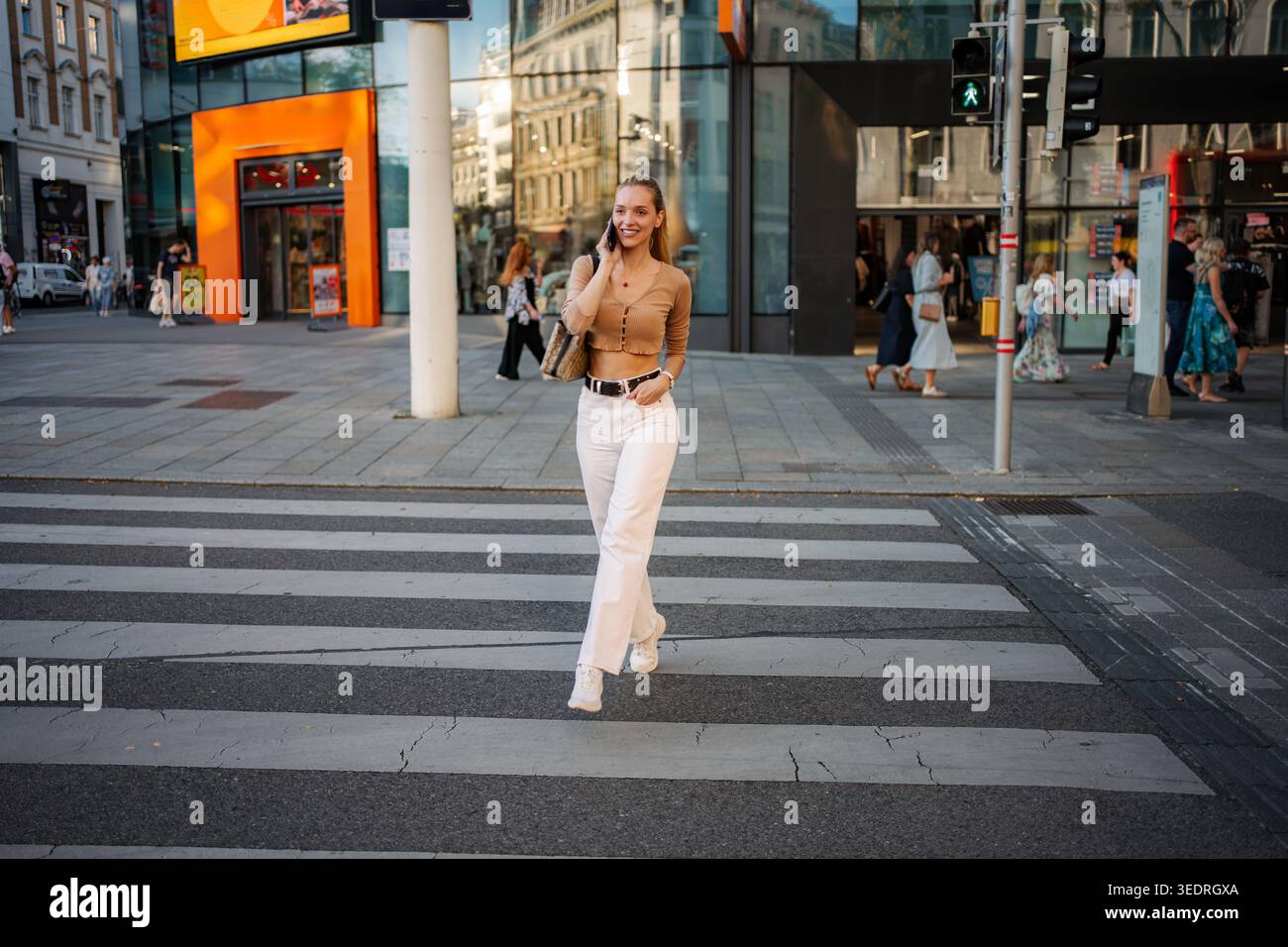 Young woman confidently talking on phone crossing Vienna street Stock Photo