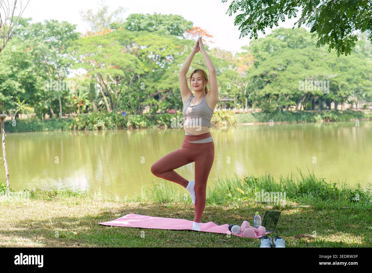 Asian woman practicing yoga tree pose in outdoor park by lake Stock ...