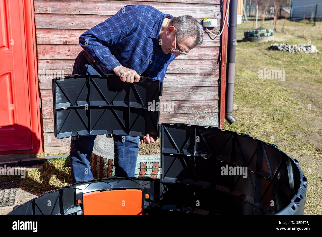 Homeowner installing compost container by joining segmented plastic panels outside. Stock Photo
