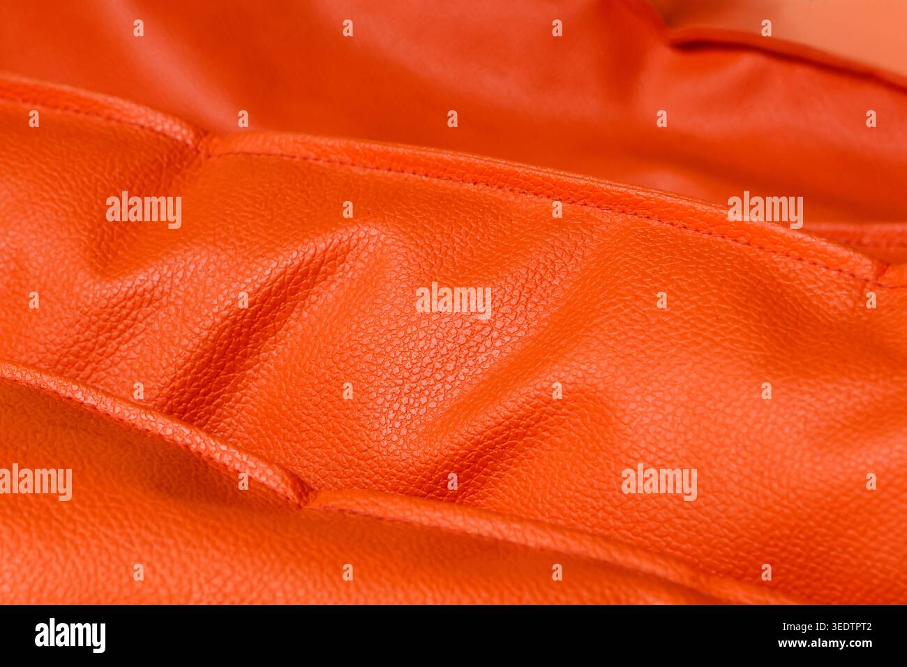 Close macro shot capturing folded bright orange leather texture creating vibrant inviting background surface highlighting premium soft fabric material Stock Photo