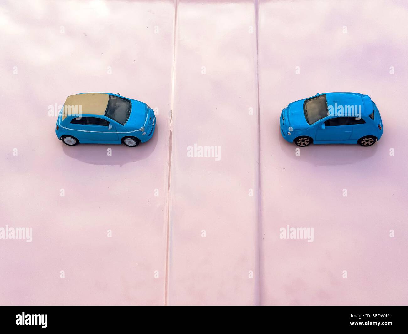High angle view of two blue miniature Fiat 500 toy cars facing each other on a pale pink classic fiat 500 bonnet hood Stock Photo