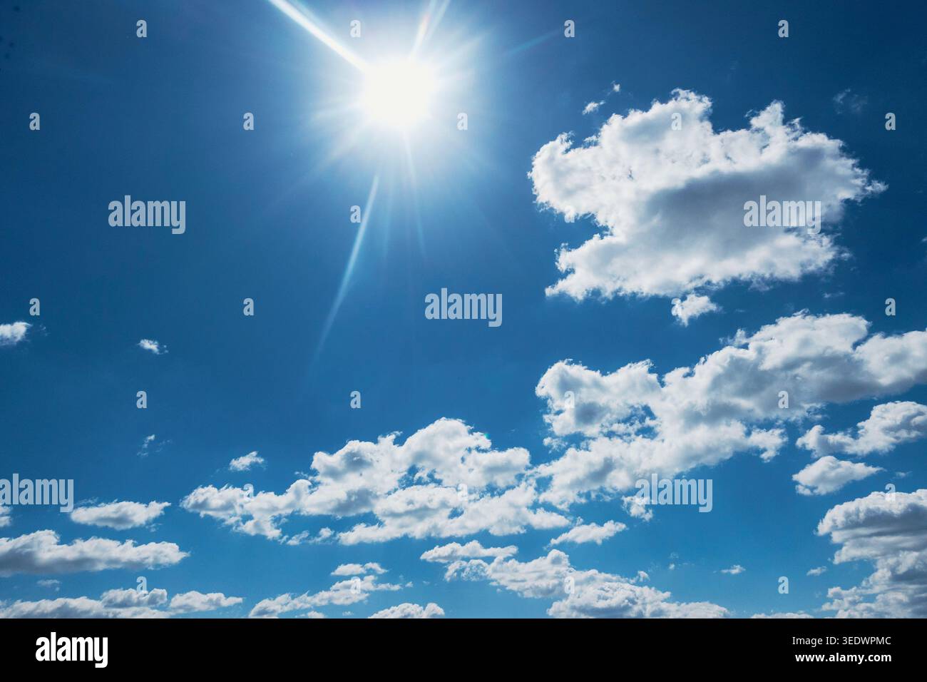 Bright sun shining in blue sky with white fluffy clouds, clear summer weather background Stock Photo